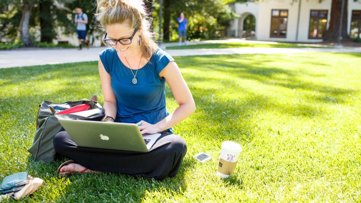 一个学生坐在草坪上用笔记本电脑学习 