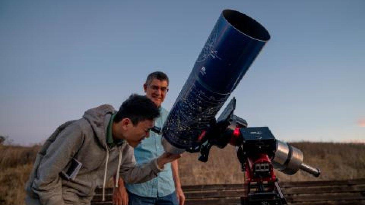 学生用大型望远镜观看夜空，教师在一旁观看