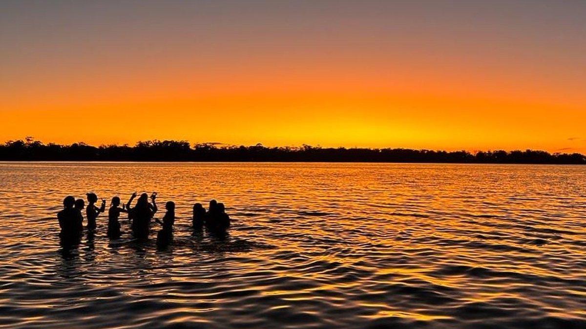 学生们站在海边，映衬着明亮的橙色夕阳.